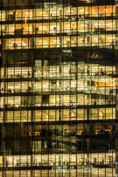 Corporate interior floors illuminate a glass office building facade at night, where urban architecture and windows form a dense grid of working spaces