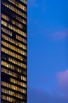 Office building windows rise against the night sky, turning urban architecture into a slim glass facade with corporate interior lights along the tower edge