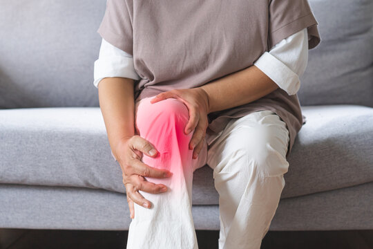 Body arthritis muscles stiff problem, aged woman suffering on leg, pain knee from disease chronic, hand massage rubbing joint injury, mature hurt or sore sitting on sofa at home. Health care people.
