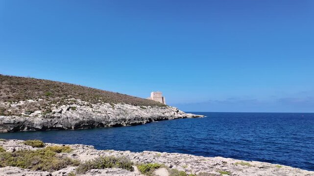 Low angle view of the Xlendi Tower standing against the azure sea and rugged coastline, creating a stunning contrast, Xlendi, Munxar, Malta. Hyperlapse. High quality 4k footage