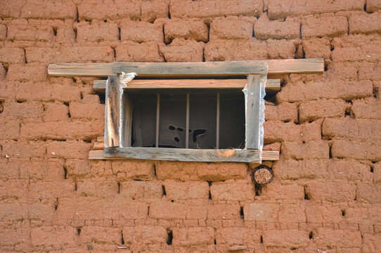 Wood-frame rectangular screen window in red-brown adobe brick wall