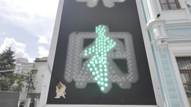 A green pedestrian traffic light glows brightly on a busy city street. The signal regulates active urban road traffic and pedestrian crossings.