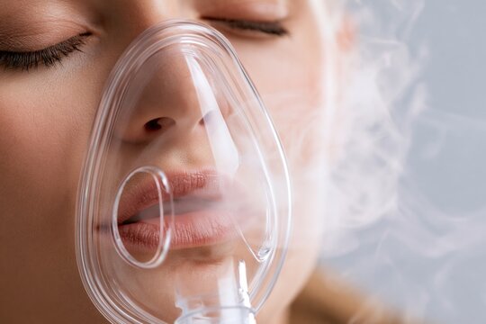 Close-up of person using home inhaler mask, gentle mist visible, calm neutral background, soft clinical lighting, healthcare and respiratory treatment concept