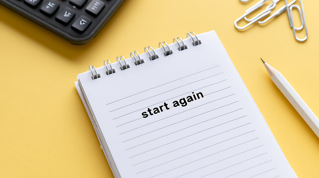 Inspiring message 'start again' on a spiral notebook with a pencil, calculator, and paper clips on a cheerful yellow background, flat lay