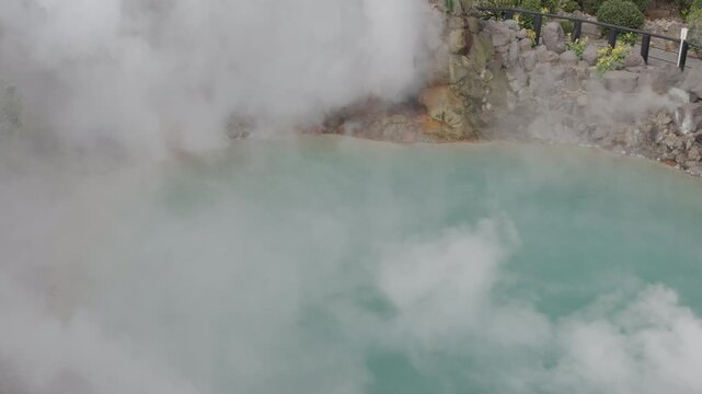 Thick hot steam and smoke blowing across a turquoise blue geothermal hot spring pond by a gentle wind. Scenic volcanic onsen landscape in Japan. Umi Jigoku, Beppu, Fukuoka