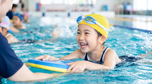 スイミングスクールでコーチから水泳を教わる小学生の子ども