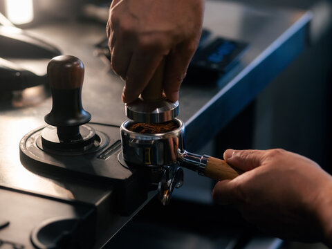 Barista tamping ground coffee in portafilter using press 