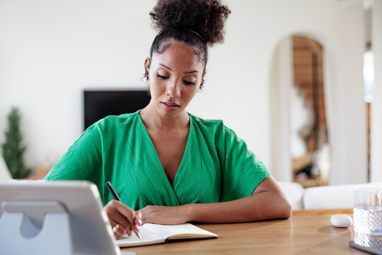 Woman in green dress writing in notebook at desk.
