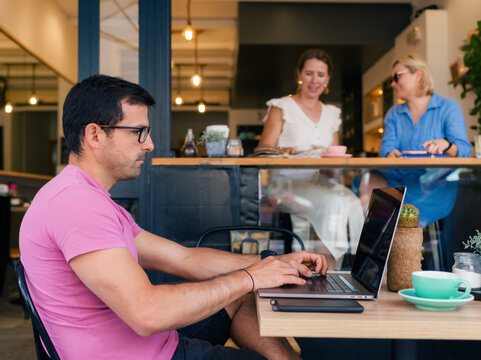Man Working on Laptop in a Cafe While Friends Chat Nearby