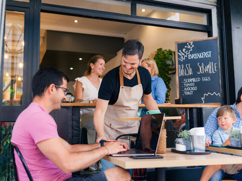 Cheerful waiter serving guests at sidewalk cafe 