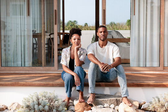 Couple sits barefoot on wooden porch of modern home.