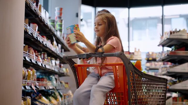 Happy little girl holds corn flakes pack sitting in shopping cart