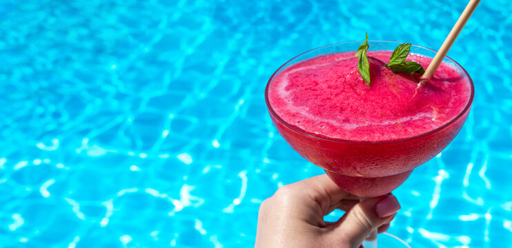 Hand holding strawberry Daiquiri by poolside on sunny day. Concept of summer relaxation and refreshing drinks