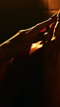 Close-up of woman gently touching neck and collarbone in warm dramatic lighting. Beauty, skincare, self care, wellness and spa relaxation concept with sensual atmosphere.