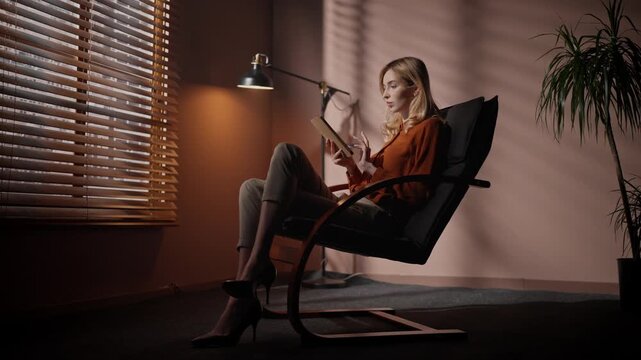 Professional woman crossing legs on office chair. Female sitting at chair at background of dim design. Woman in official suit sitting at dark room. Female director holding tablet at audition room.