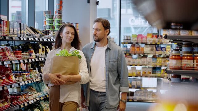 Couple with paper bag of goods walks along aisle in grocery