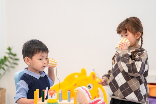 Children play with toy cups and strings in a classroom while talking to each other