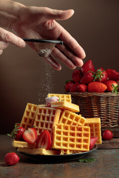 The chef sprinkles powdered sugar on the waffles topped with fresh strawberries.
