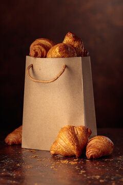 Fresh croissants in paper bag on a brown vintage table.