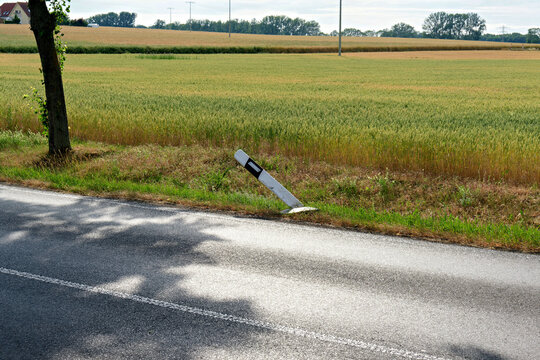 Tilted road delineator post on roadside next to agricultural wheat field