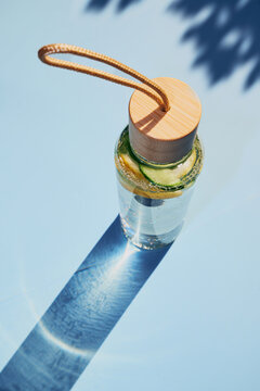 Glass water bottle with water, lemon, cucumber and blueberries on blue background under sunlight