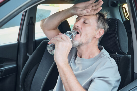 Man suffering from heat and thirst, drinking bottled water to hydrate inside car