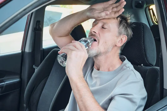 Man suffering from heat and thirst, drinking bottled water to hydrate inside car