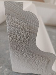 A close-up shot showing the detailed cross-section of a white decorative cornice or crown molding, highlighting the textured inner material and the smooth shaped exterior. Ideal for showcasing constru © Коротун Микола