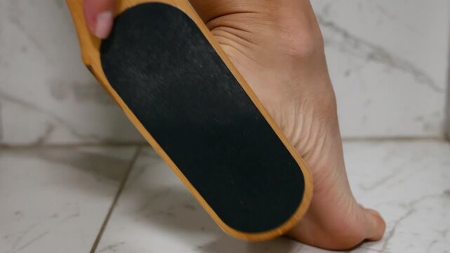 Close-up of woman removing callus from dry cracked heel with foot file for smooth healthy feet