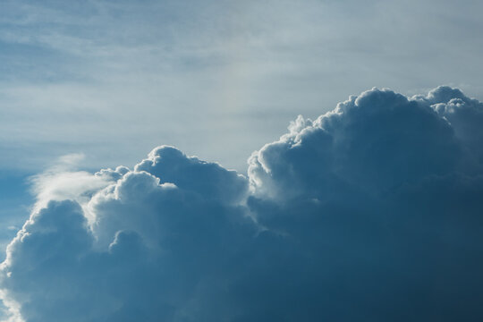 Dark gray clouds with white edges illuminated by sunlight against a blue sky, creating a dramatic and textured atmosphere in the background