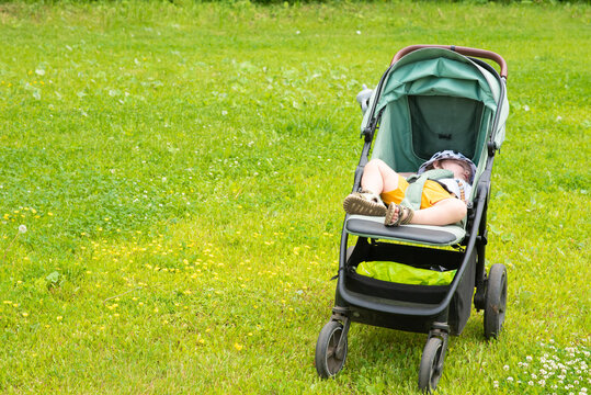  Small toddler boy sleeping inside stroller on green grass outdoors