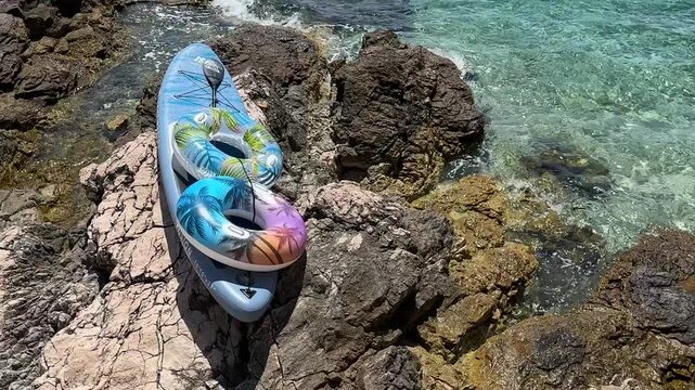 Kayak resting on rocks near clear water with colorful floaties in sunlight