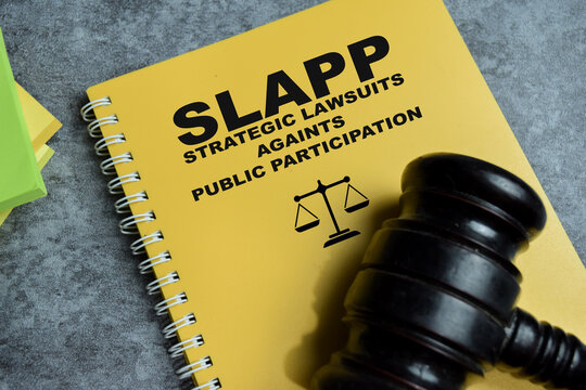 Concept of SLAPP - Strategic Lawsuits Against Public Participation write on book isolated on Wooden Table. For legal pressure on free speech and silencing critics
