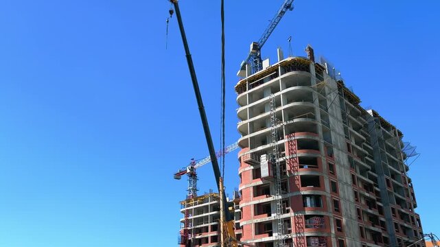 High-rise residential building under construction with elevator rising and tower crane against clear blue summer sky
