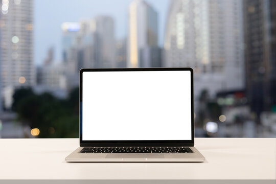 close up blank white screen display of laptop computer on table in office building with cityscape scene for add content of design banner,website or template or online shopping e-commerce concept