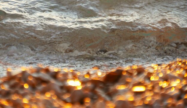 Beach with glowing pebbles by the sea with waves splash in golden sunset, summer beach background