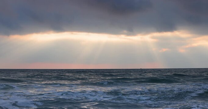 sea sunrise sunbeams breaking through dramatic dark clouds over stormy ocean sea waters