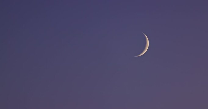 Thin crescent moon shining in the dark twilight sky with stars
