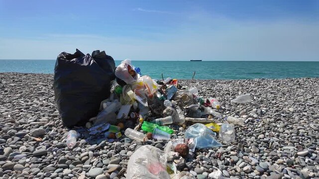 Plastic waste and other rubbish piled up on a pebble beach, contaminating the shoreline while a cargo ship sails on the distant sea, symbolizing a serious environmental problem and pollution