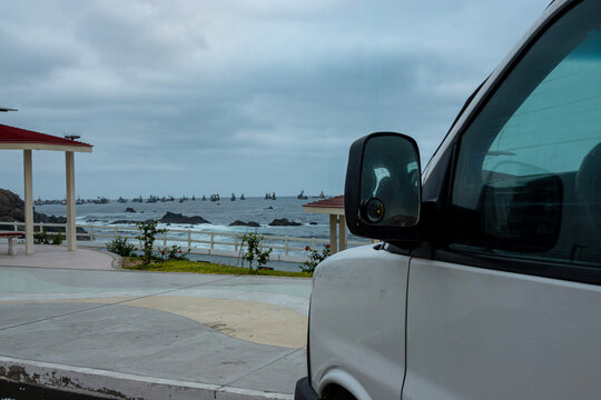 White camper van parked beside the Pacific Ocean with fishing boats on the horizon in Ilo, Peru