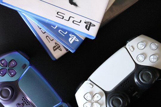 PlayStation 5 games software cases with DualSense controllers on dark background. Next-gen video gaming console ecosystem, esports entertainment, physical media discs and industry trends.