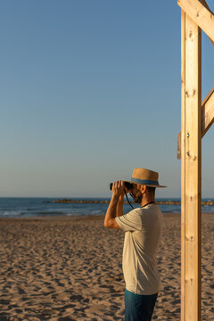 Vertical man using binoculars on sunny beach