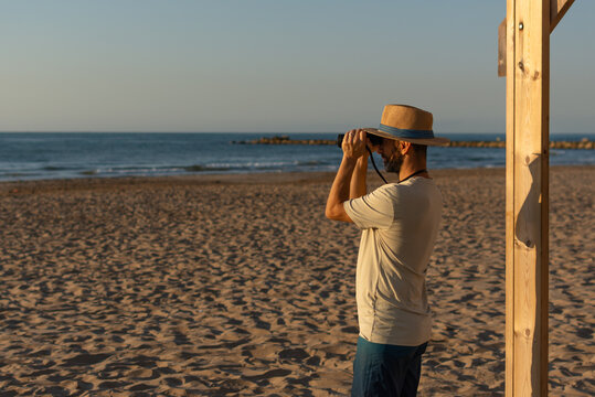 man using binoculars on sunny beach during morning