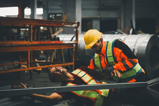 Workplace accident and industrial safety concept. Factory worker assisting injured coworker after a workplace incident in a manufacturing facility. Safety, emergency, first aid, prevention, industry