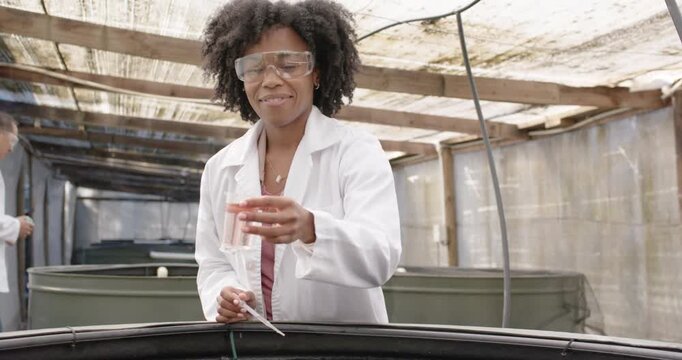 African woman in white coat conducting water sampling during monitoring, filling vial in hatchery