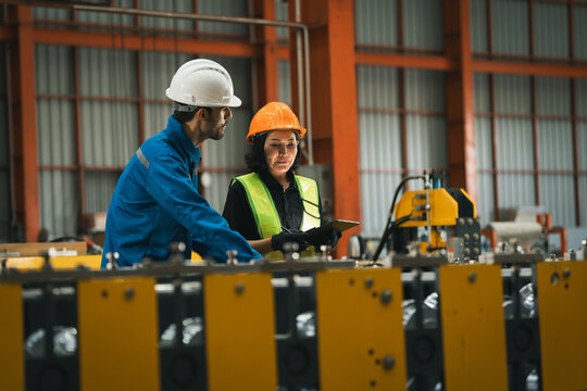 two professional engineer, worker, technician use clipboard discuss work, walk in steel metal manufacture factory plant industry. engineering man and woman wear hard hat check quality machine