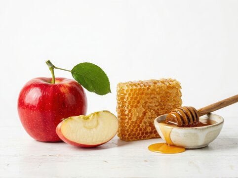 Fresh red apple with green leaf and a piece of honey in honeycomb with a small bowl of liquid honey and wooden dipper isolated on white background