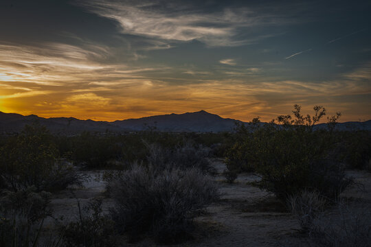 Scenic desert landscape at twilight with dark mountain silhouettes under a vibrant warm dusk sky.