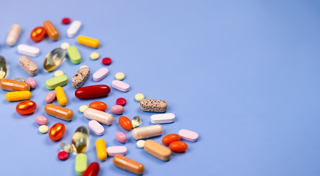 Assorted colorful vitamins, capsules, tablets, and supplements on a blue background with copy space. Concept of healthcare, nutrition, wellness, pharmacy, and preventive medicine.