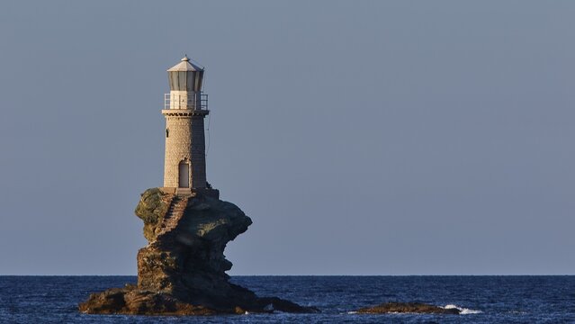 Telephoto shot, white round lighthouse on rock close, sea dark blue, sky light blue and cloudless, Andros town, Chora, Andros island, Cyclades, Greece